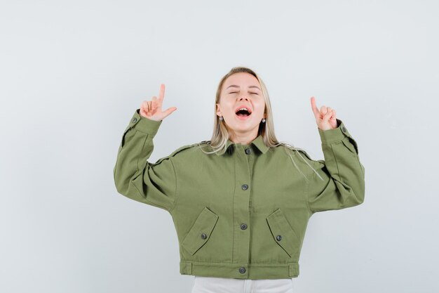 Free photo young female pointing up while screaming in green jacket,jeans , front view.