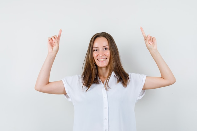 Young female pointing up in white blouse and looking cheery.