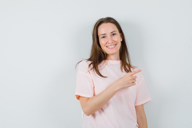 Young female pointing at upper right corner in pink t-shirt and looking happy. front view.