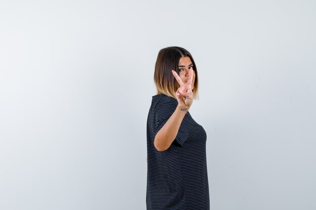 Young female in polo dress showing victory sign and looking pretty , front view.