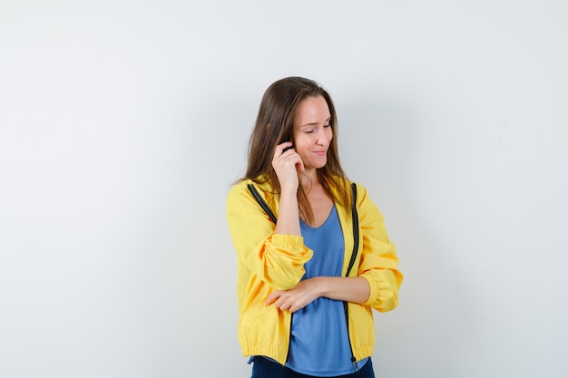 Young female posing while thinking in t-shirt, jacket and looking optimistic. front view.