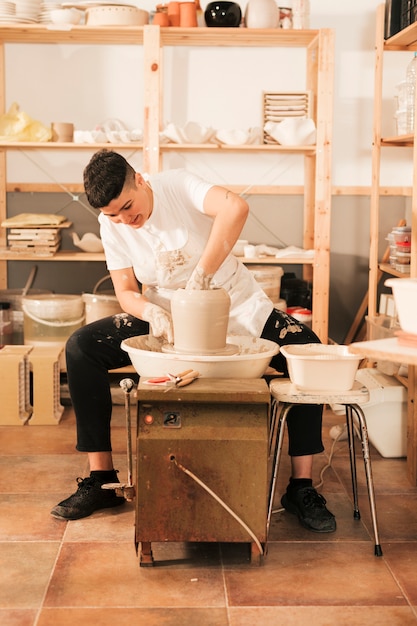 Free Photo a young female potter sculpting on a potter's wheel in the workshop