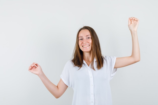 Young female raising arms while smiling in white blouse and looking happy