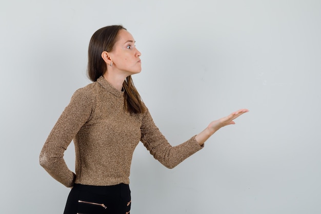 Young female raising hand with open palm aside in golden blouse and looking aggressive. .