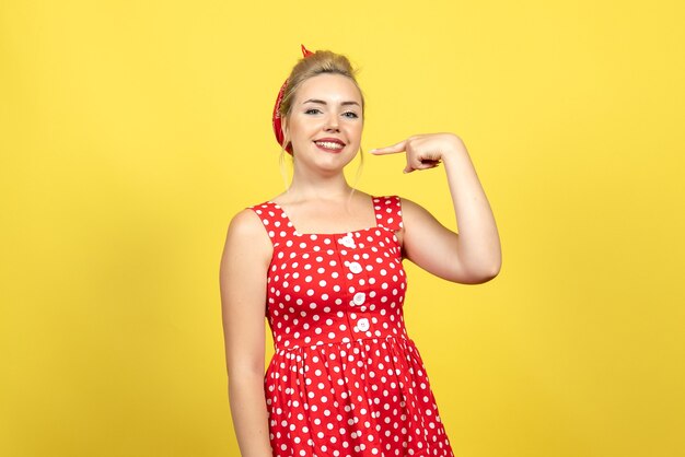 young female in red polka dot dress posing on yellow