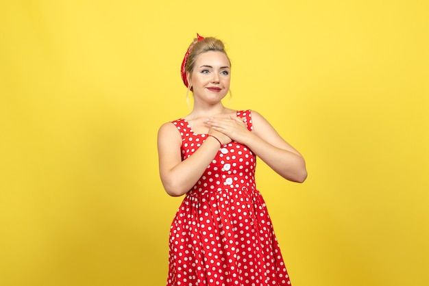 young female in red polka dot dress smiling on yellow