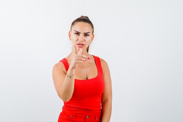 Young female in red tank top, pants pointing at camera and looking confident , front view.