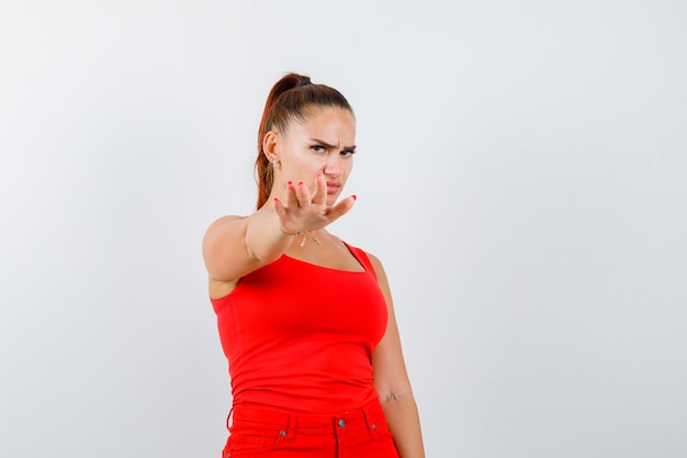 Young female in red tank top, pants showing stop gesture and looking scared , front view.