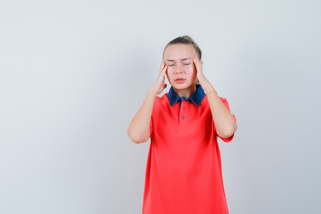 Young female rubbing temples and having headache in t-shirt front view.