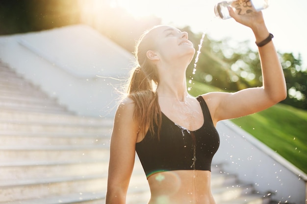 Young female runner pouring water over herself after a long and hard morning workout Urban sport and lifestyle concept