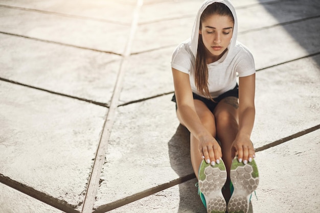 Free photo young female runner stretching before starting a run of her life in urban environment sports make us stronger