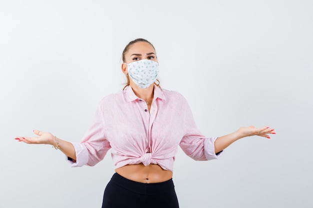 Free Photo young female in shirt, pants, mask showing helpless gesture and looking puzzled , front view.