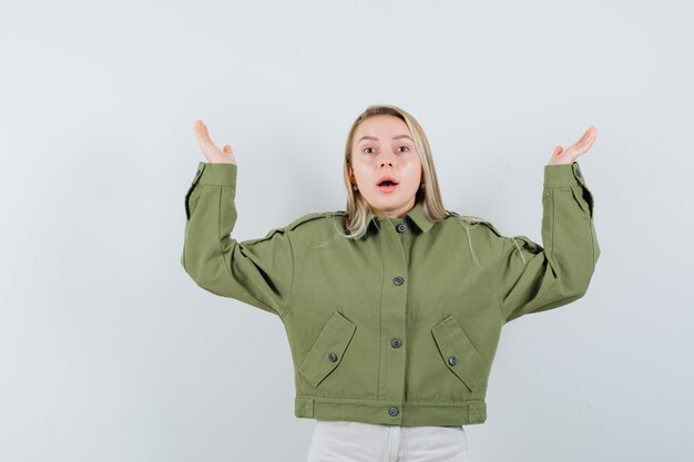 Free photo young female showing helpless gesture in green jacket,jeans and looking troubled. front view.