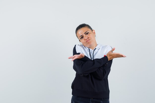 Young female showing helpless gesture with crossed arms in colorful sweatshirt and looking anxious. front view.