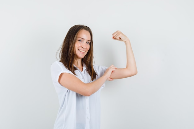 Young female showing her arm muscles in white blouse and looking powerful