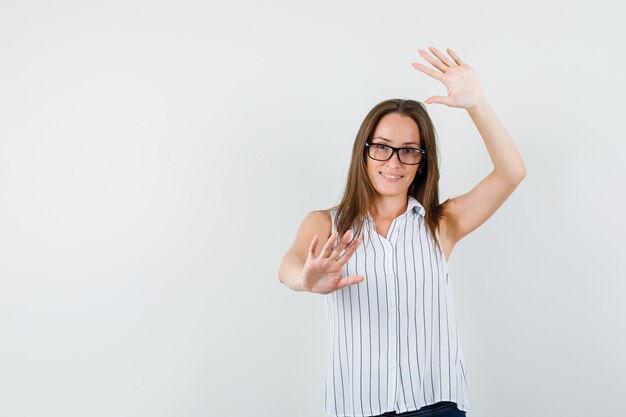 Young female showing raised palms in t-shirt, jeans and looking funny , front view.