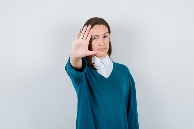 Young female showing stop gesture in sweater over shirt and looking serious. front view.