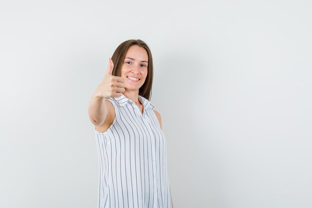 Young female showing thumb up in t-shirt and looking cheery , front view.