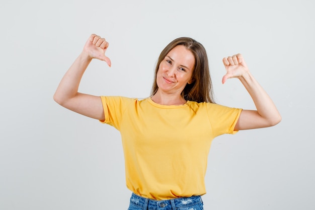 Free photo young female showing thumbs down in t-shirt, shorts and looking displeased. front view.