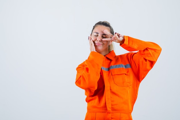 Free photo young female showing v-sign over her eye in worker uniform and looking beloved. front view.