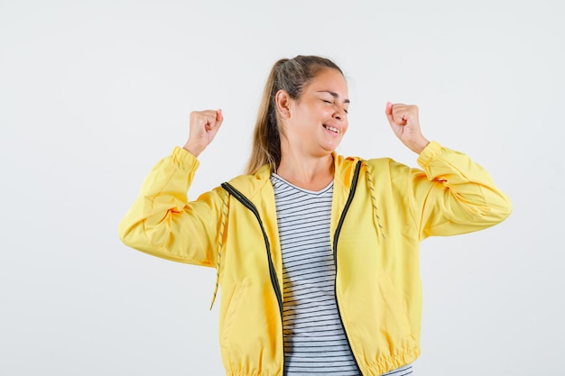 Young female showing winner gesture in jacket, t-shirt and looking happy. front view.