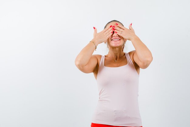 Young female in singlet closing eyes with hands and looking cute , front view.