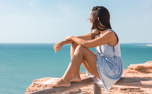 Young female sitting on a plank and watching the sea at daytime