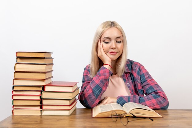 young female sitting with books and reading on white