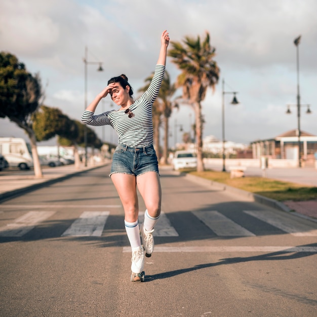 Young female skater with her arm raised dancing on road