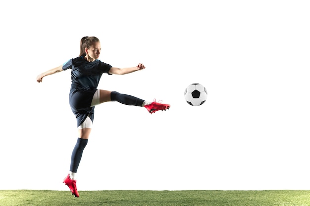 Free photo young female soccer or football player with long hair in sportwear and boots kicking ball for the goal in jump isolated on white background. concept of healthy lifestyle, professional sport, hobby.