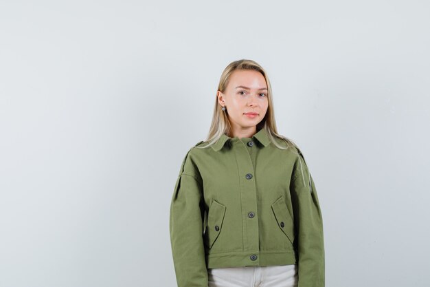 Young female standing in green jacket and looking calm , front view.