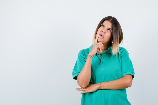 Young female standing in thinking pose in polo t-shirt and looking puzzled , front view.