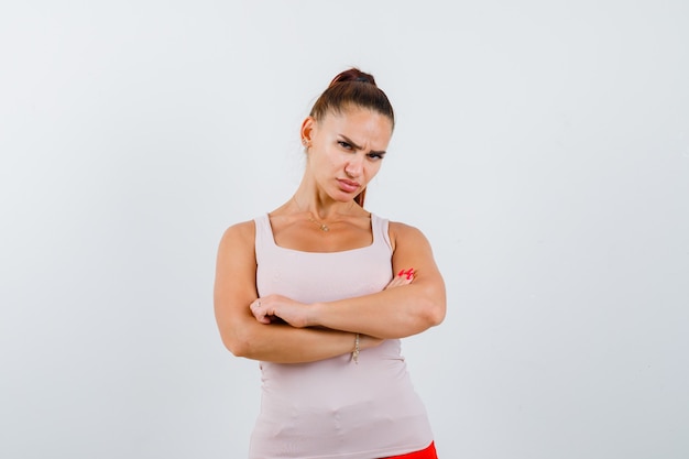 Young female standing with crossed arms in white tank top and looking confident , front view.