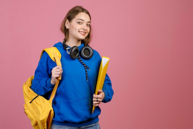 Young female student holding yellow rucksack and folder smiling