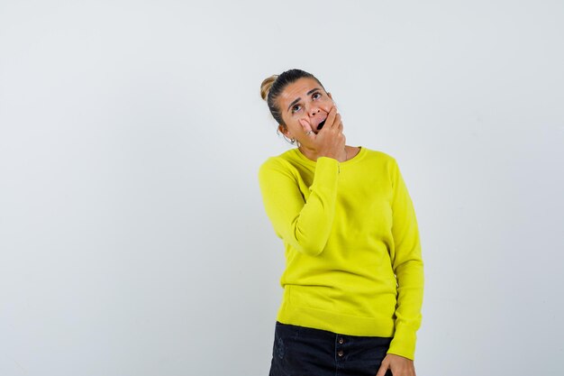 Young female in sweater, denim skirt covering mouth with hand and looking amazed 