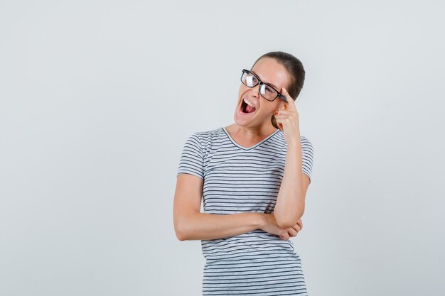 Young female in t-shirt, glasses yawning while looking away and looking pensive , front view.