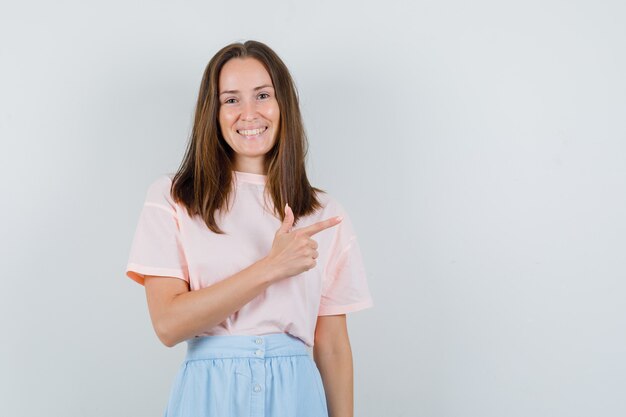 Young female in t-shirt, skirt pointing to side and looking positive , front view.