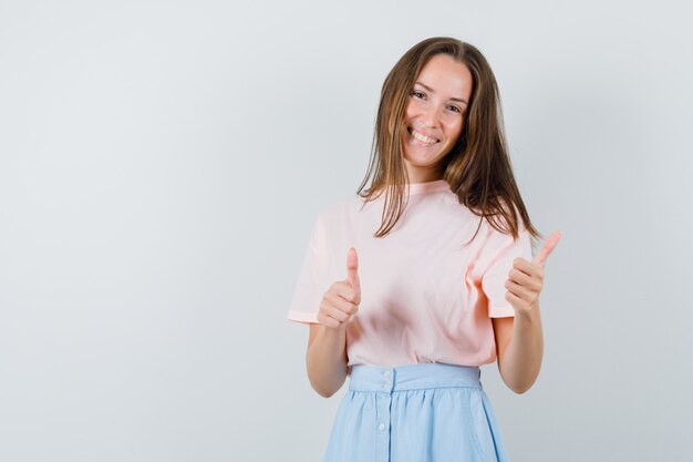 Young female in t-shirt, skirt showing thumbs up and looking lucky , front view.