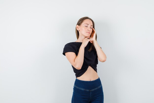 Young female touching temples and chin in black blouse, pants and looking relaxed