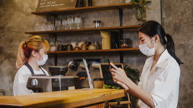 Young female wear face mask self service use mobile phone pay contactless at restaurant.