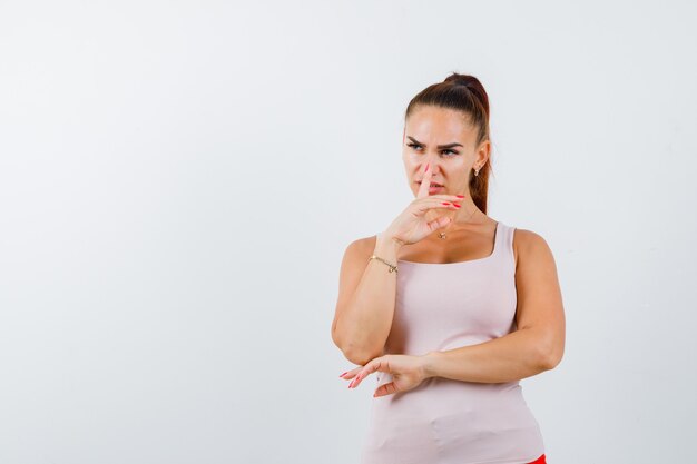 Young female in white tank top showing silence gesture and looking confident , front view.