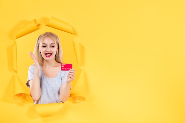 Free photo young female with credit card on a torn yellow paper background money bank shopping