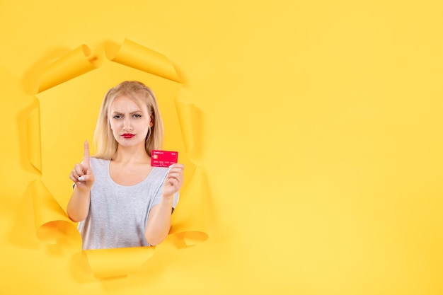 Free photo young female with credit card on torn yellow paper surface money bank shopping