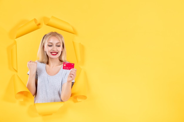 Young female with credit card on a torn yellow paper surface