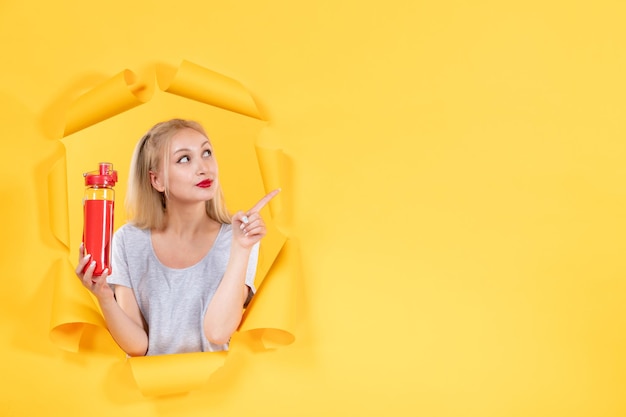 Young female with red bottle on yellow wall