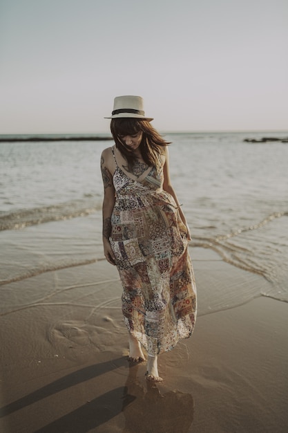 Free photo young female with tattoos wearing a dress and straw hat on blurred ocean