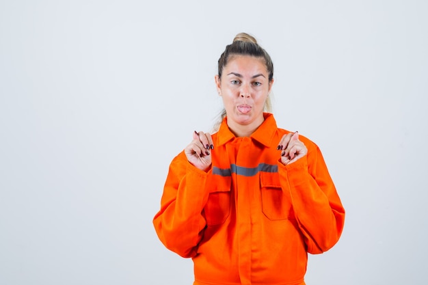 Free photo young female in worker uniform showing fig gesture,sticking out tongue and looking crazy , front view.