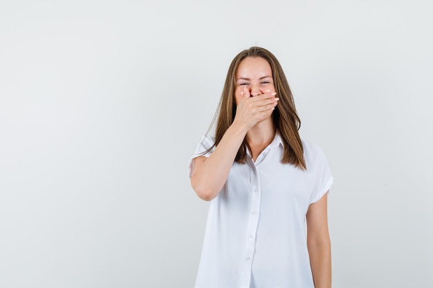 Young female yawning mouth with her hand in white blouse and looking jaded