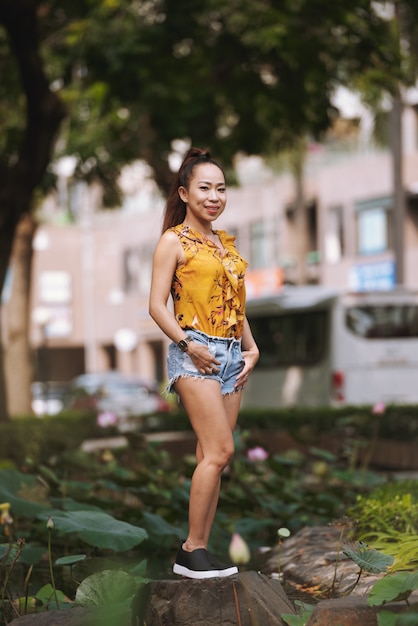 Free photo young fit fashionably dressed asian woman in shorts and bright blouse posing in urban street