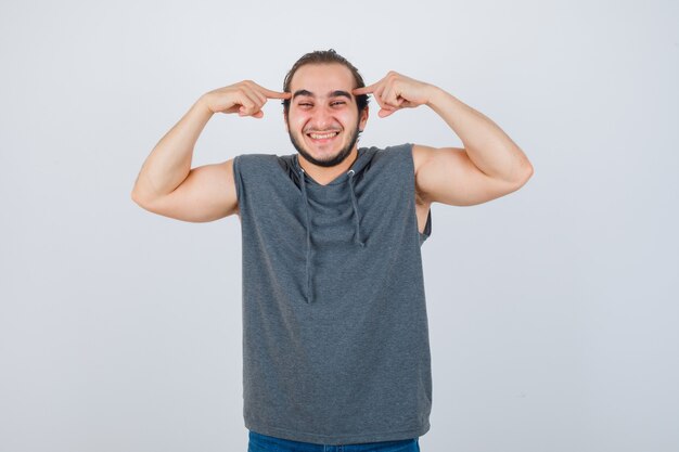 Young fit male keeping fingers on temples in sleeveless hoodie  and looking blissful. front view.